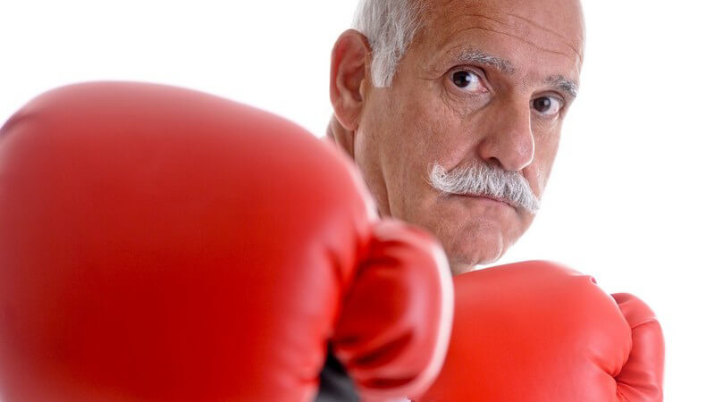Älterer Mann mit grauen Haaren und Schnurrbarrt mit roten Boxhandschuhen