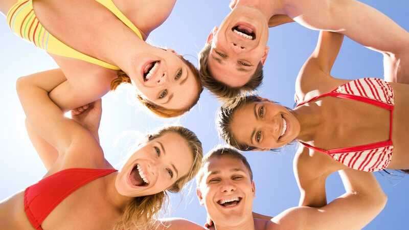 Fünf Jugendliche in Badekleidung (Bikini Badehose) stehen im Kreis und blicken nach unten in die Kamera, Sonne, Fröhlich