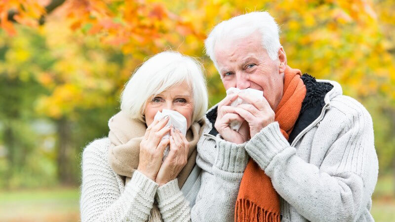 Erkältetes Seniorenpaar putzt sich im herbstlichen Park die Nase