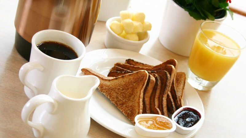 Frühstückstisch mit Toasts, Kaffee, Sahne, Orangensaftglas, Marmelade auf Holztisch
