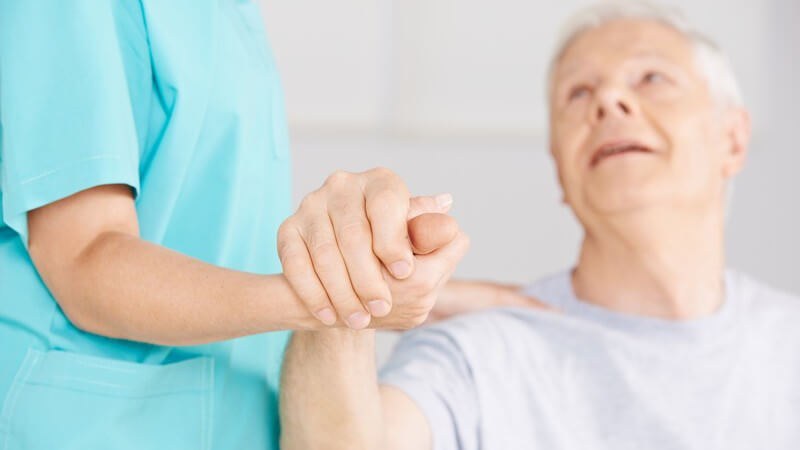 Krankenpflegerin grünem Kittel hält die Hand eines alten Mannes