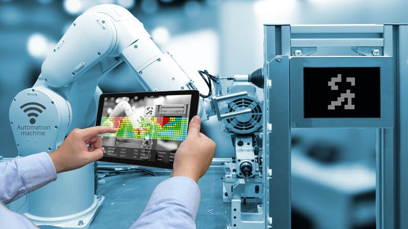 Mann bedient ein Tablet vor einem Roboterarm einer Maschine in einer modernen Fabrik