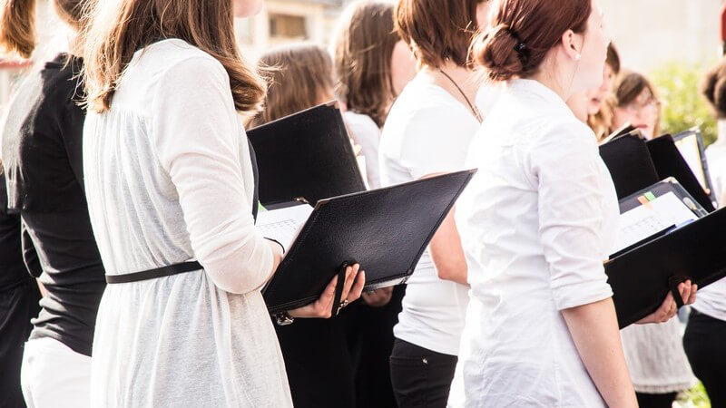 Junge Frauen in schwarz-weißer Kleidung halten ein Gesangsbuch und singen im Chor