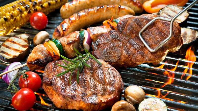 Grillrost voll mit Steaks, Spießen, Würstchen und Gemüse