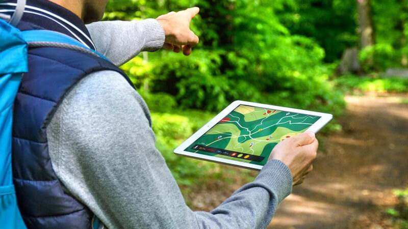 Mann wandert mit Tablet-PC und Wander-App durch einen Wald
