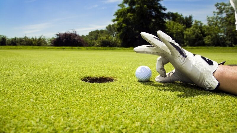 Golfloch, Golfball und Hand mit Golfhandschuhen, Zeigefinger und Daumen zum Kreis geformt
