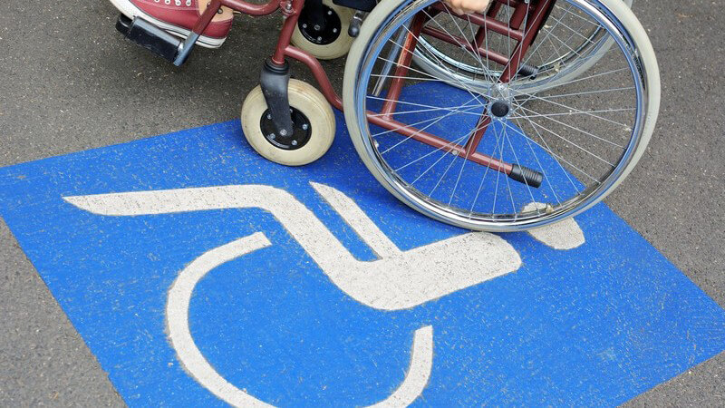 Großes blaues Behindertenparkplatz-Zeichen auf Asphalt, darauf ein Rollstuhlfahrer