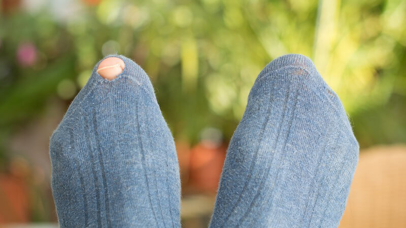 Füße in grauen Socken, der linke Socken hat ein Loch