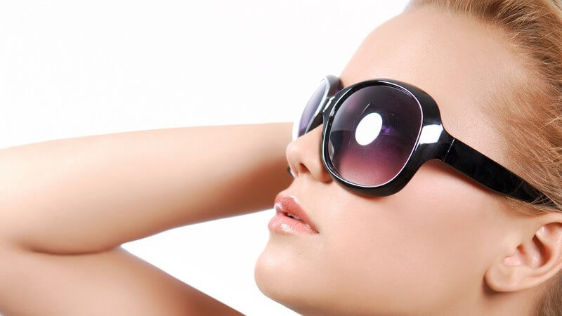 Seitenansicht junge Frau trägt Sonnenbrille mit großen Gläsern und schaut nach oben