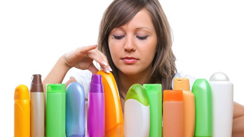 Junge Frau hinter einer großen Sammlung von Kosmetika wie Duschgel und Shampoo