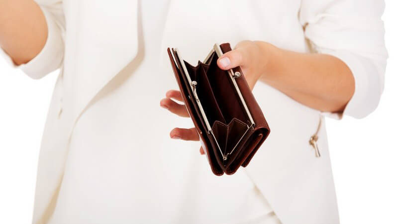 Frau in hellem Blazer hält eine leere Geldbörse vor weißem Hintergrund