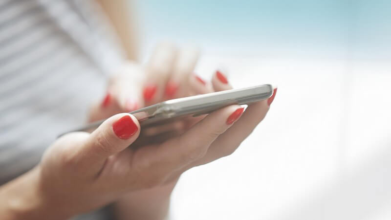Frau mit roten Fingernägeln bedient ein Smartphone