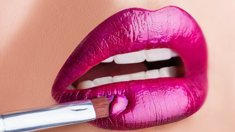 Frau trägt lila Lipgloss mit einem Pinsel auf die Lippen auf (Nahaufnahme)