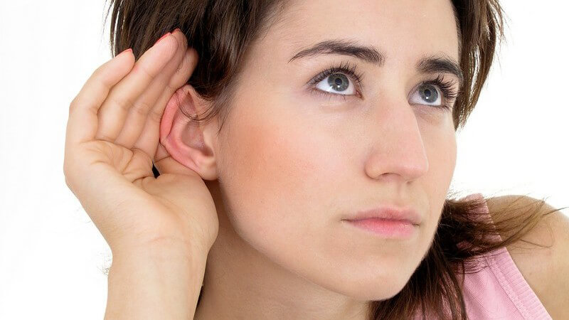 Junge Frau hält Hand hinters Ohr um besser zu hören, weißer Hintergrund
