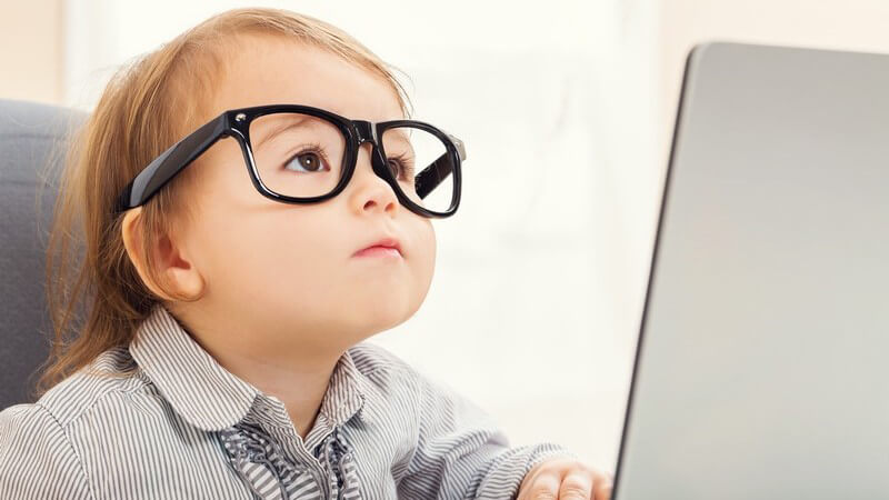 Kleines Mädchen mit großer Hornbrille sitzt vor einem Laptop