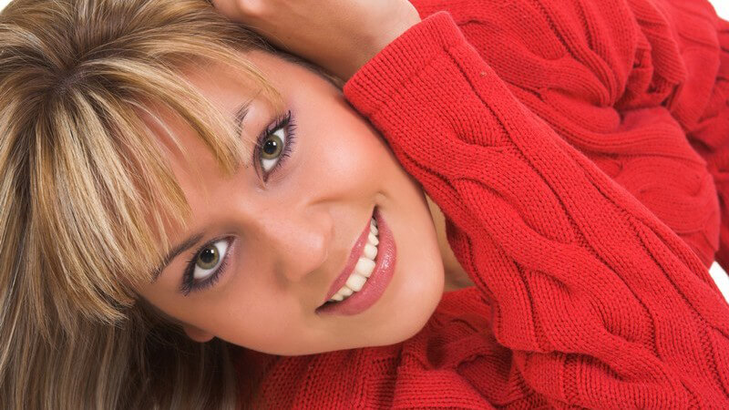 Junge blonde Frau in rotem Strickpullover lächelt in Kamera