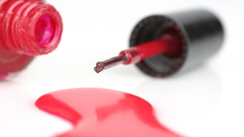 Roter ausgelaufener Nagellack, daneben umgekippte Nagellackflasche und Pinsel