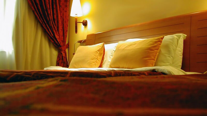 Hotelzimmerbett mit gelben Kissen und brennender Nachttischlampe an der Wand