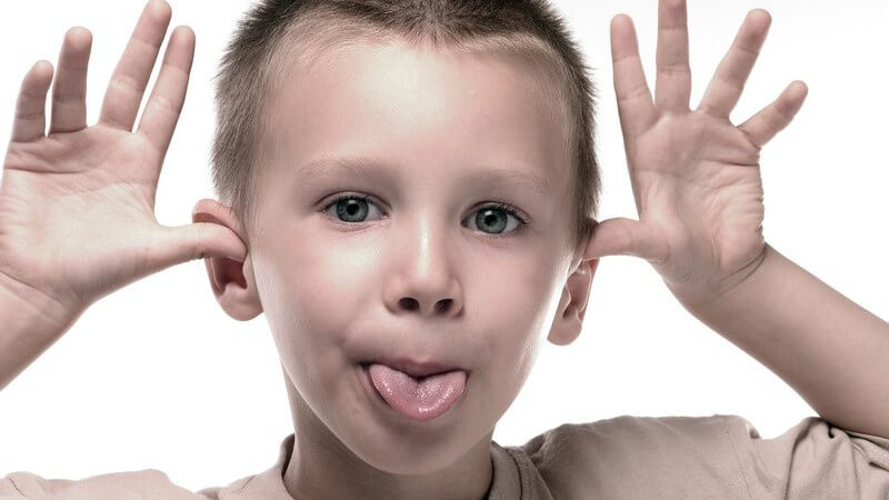 Junge hält Hände an Ohren, Handflächen nach vorn, streckt Zunge raus