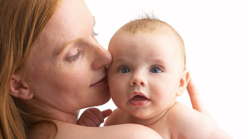 Mutter hält Baby im Arm, küsst es auf Wange