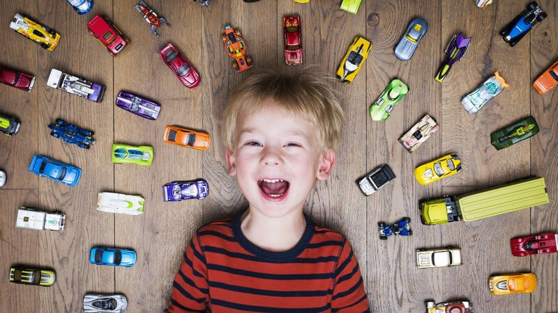 Junge liegt auf dem Boden, umringt von zahlreichen Spielzeugautos