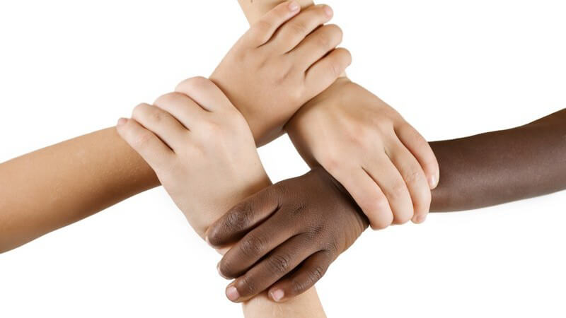 Drei weiße und eine schwarze Kinderhand halten sich gegenseitig am Handgelenk fest