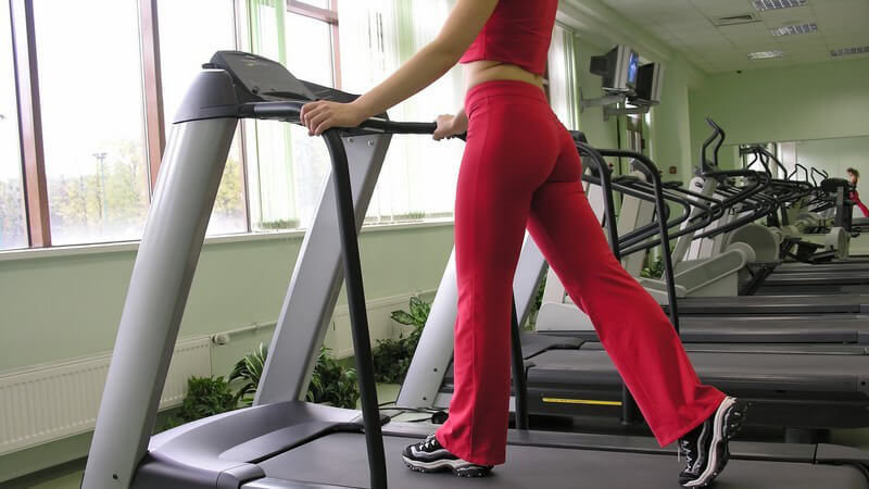 Unterkörper einer Frau im roten Sportoutfit im Fitnessstudio auf Laufband