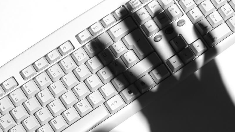 Weiße Computer Tastatur, darüber Schatten der rechten Hand