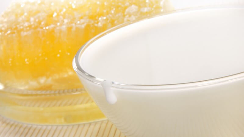 Glasgefäß mit Milch vor einer gelben Honigwabe