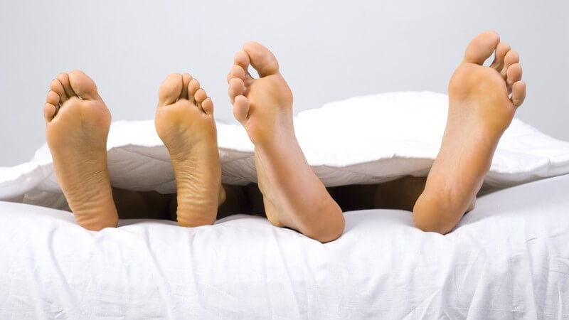 Zwei Paar nackte Füße schauen unter einer weißen Decke hervor