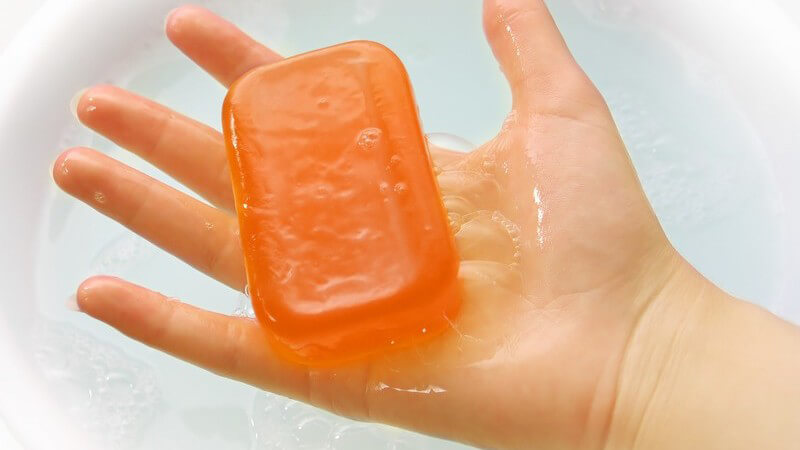 Rechte nasse Hand hält orange Seife, darunter Wasser