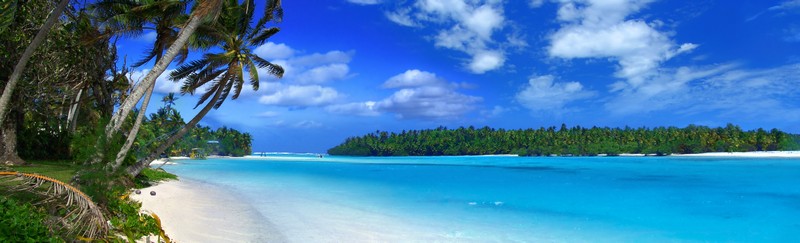 Panorama von Lagune mit Palmen im linken Vordergrund, weißem Strand und azurblauem Meer