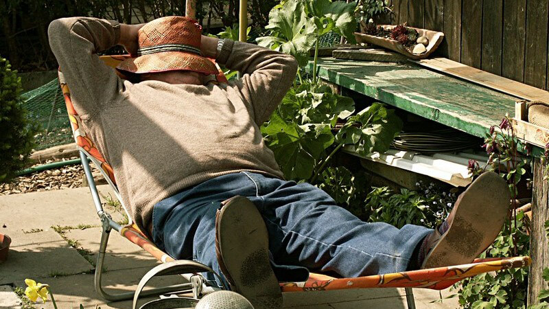Mann ruht sich auf einem Liegestuhl mit Hut überm Gesicht im Garten aus