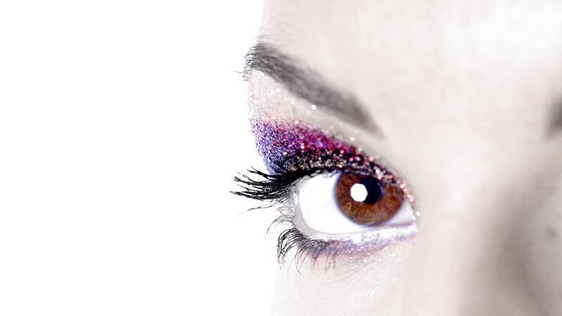 Braunes Auge mit glitzerndem Lidschatten in lila und pink