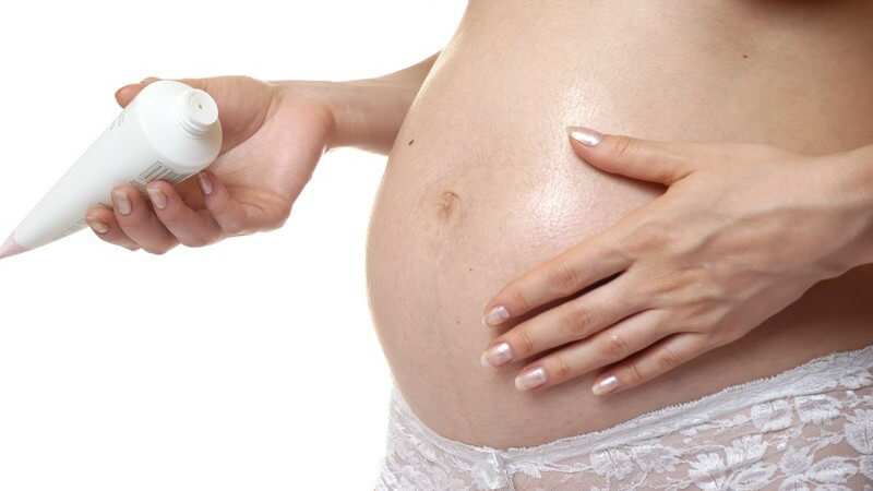 Schwangere Frau cremt ihren Bauch ein