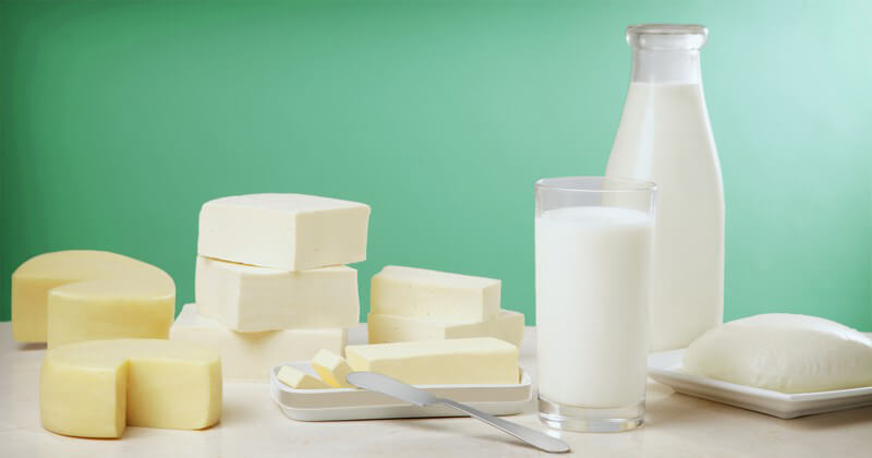 Milch in Glasflasche und Glas, daneben Milchprodukte wie Butter und Käse
