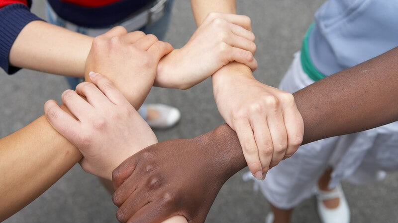 Multikulti Hände von Jugendlichen mit verschiedener Hautfarbe fassen sich zu einem Kreis oder Stern