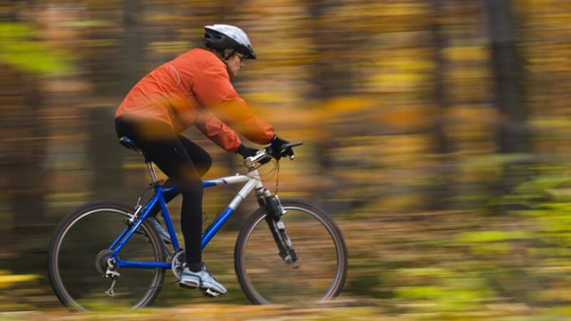 Sportlich angezogene Frau mit Fahrradhelm fährt auf Mountainbike im Wald