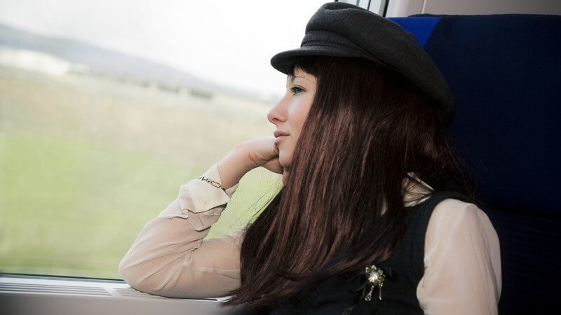 Junge Frau mit Hut schaut während einer Bahnfahrt aus dem Fenster