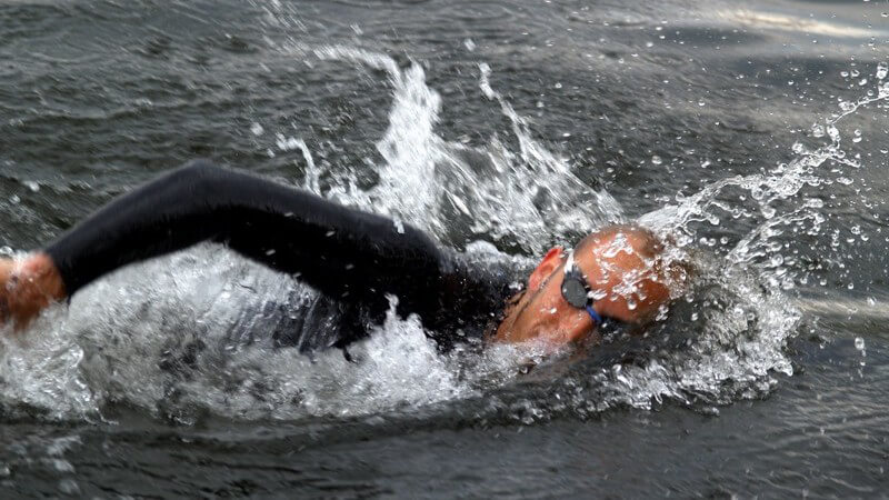 Schwimmer in Anzug und Schwimmbrille krault im freien Gewässer
