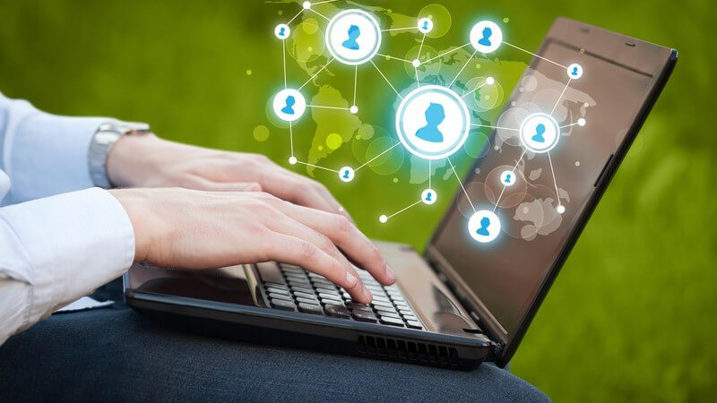 Hände auf Tastatur eines Laptops, über dem vernetzte Social Media-Avatare schweben, grüner Hintergrund