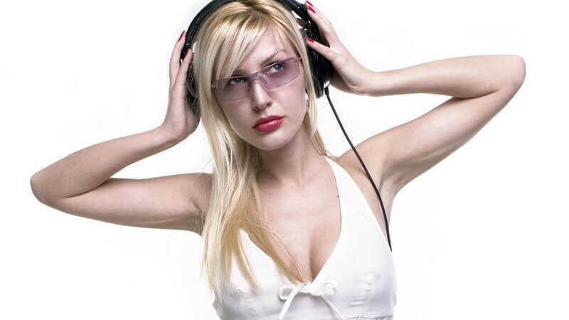 Blonde Frau mit getönter Brille und weißem Top hört Musik über Kopfhörer