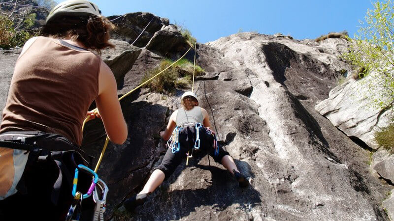 Ansicht von unten: Zwei Freundinnen beim mit Kletterausrüstung beim Klettern an einer Bergwand
