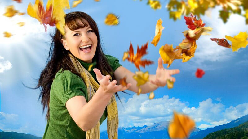 Junge Frau draußen wirft mit Herbstblättern
