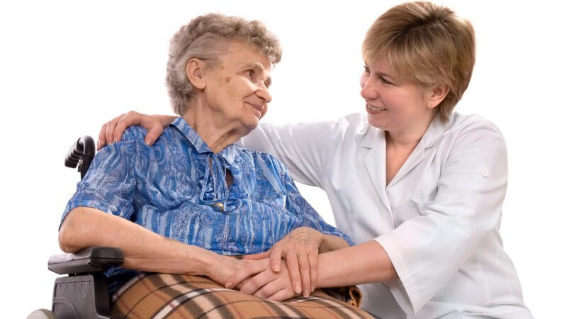 Alte Frau im Rollstuhl wird von Pflegerin betreut
