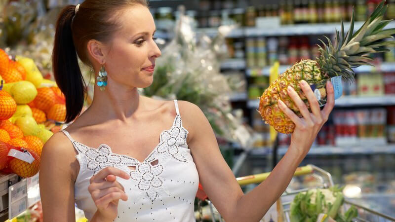 Junge dunkelhaarige Frau im Supermarkt hält Ananas in der Hand