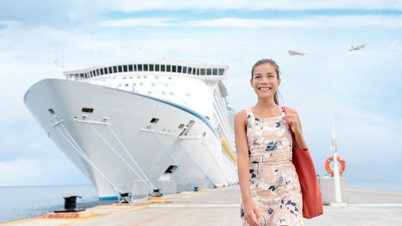 Großes weißes Kreuzfahrtschiff liegt im Hafen, junge Frau in Sommerkleid geht shoppen
