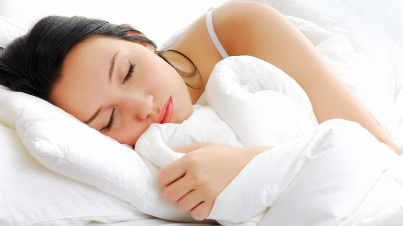 Dunkelhaarige, schlafende Frau in weißer Bettdecke liegend