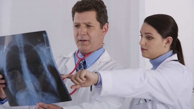Arzt hält Röntgenbild eines Brustkorbes, junge Ärztin zeigt auf das Bild, mit Kittel, Stetoskop und weißem Hintergrund