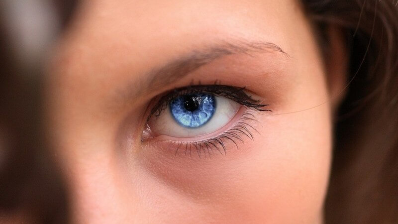 Blaues, weibliches Auge im Mittelpunkt, rechts brünette Haarsträhne hinterm Ohr